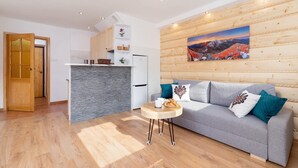 A modern living room with a grey sofa, wooden accents, a stone backsplash, and a painting of a mountain landscape.