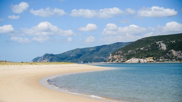 Une plage au rivage incurvé, bordée d’une eau d’un bleu limpide, avec des montagnes qui se dessinent à l’horizon.
