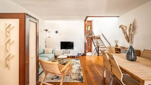 Un salon moderne avec une table à manger en bois, des chaises en osier, un téléviseur à écran plat et un escalier menant à un niveau supérieur.