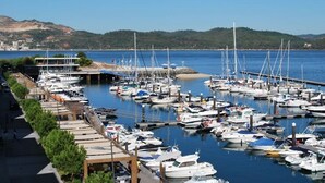 Un port de plaisance où sont amarrés de nombreux bateaux, une promenade piétonne et, en arrière-plan, des collines.
