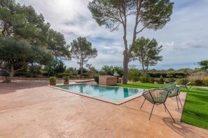 A swimming pool with a patio area, surrounded by trees and a well-maintained lawn.