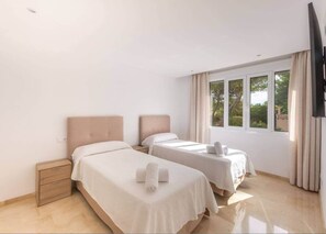 Une chambre d’hôtel avec deux lits, une table de chevet, une télévision et une fenêtre avec des rideaux.