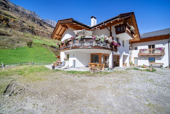 A two-story chalet with a balcony, outdoor seating, and a mountain backdrop. - Apartment "Edelweiß" with Slope Access, Private Terrace & Wi-Fi (Pfelders)