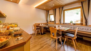 Un área de desayuno con mobiliario de madera, un bufé con diversas opciones de comida y una ventana con cortinas.