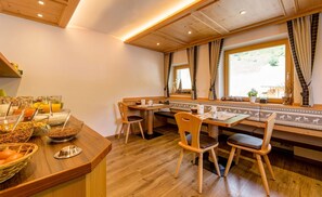Un área de desayuno con mobiliario de madera, un bufé con diversas opciones de comida y una ventana con cortinas.