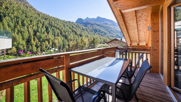 Una terraza de madera con una mesa y sillas, con vistas a una montaña boscosa.