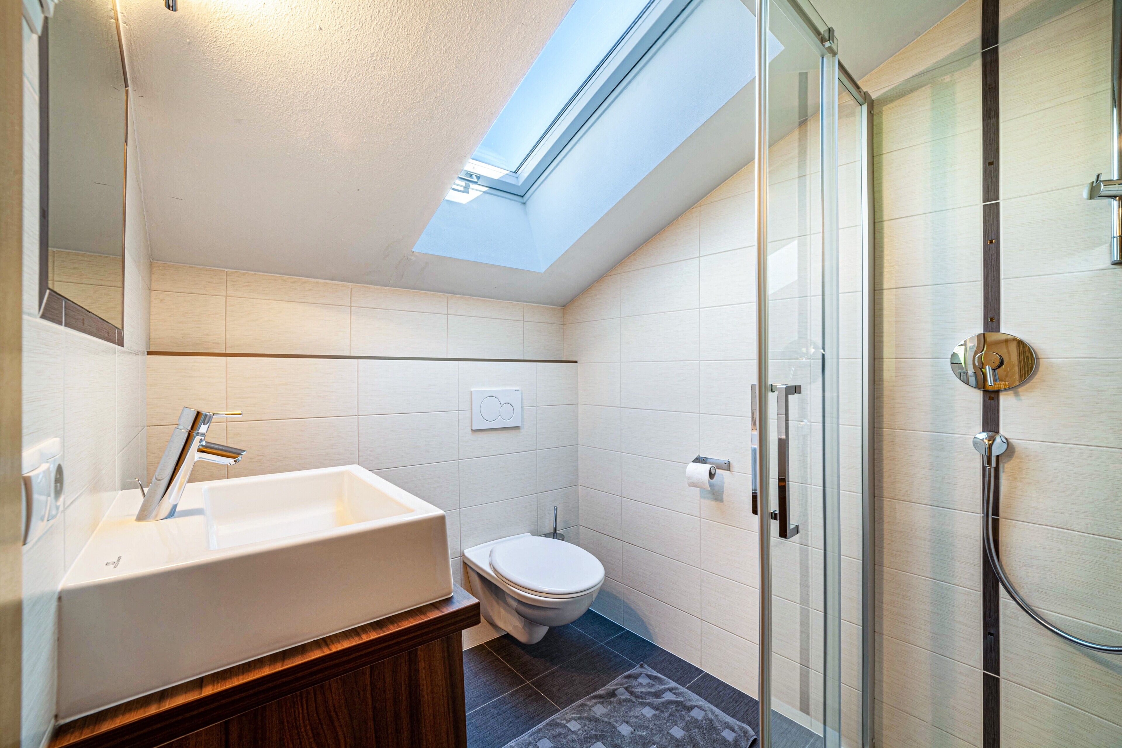 A modern bathroom with a skylight, a freestanding bathtub, a toilet, and a glass-enclosed shower.
