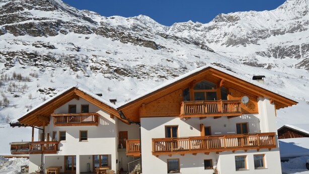 A two-story chalet with balconies, a ski lift, and a snowy mountain backdrop.