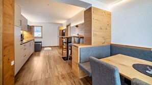 A compact kitchen with wooden cabinets, a dining area with a bench, and a small table.