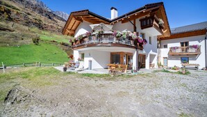 A two-story chalet with a balcony, outdoor seating, and a mountain backdrop.