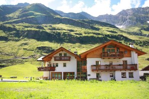 Een chalet met twee verdiepingen en balkons, gelegen tegen een bergachtige achtergrond.