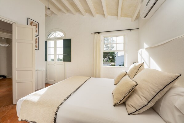 Ein Schlafzimmer mit Bett, einem fensterbelaubten Fenster, einer Tür und einer Wand-Klimaanlage.
