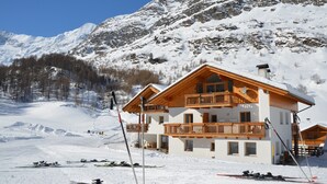 A chalet-style hotel with a wooden balcony, ski equipment, and a mountainous backdrop. - Apartment 'Lazins' with Private Terrace & Wi-Fi (Pfelders)
