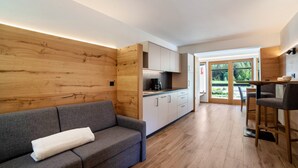 A modern interior with a grey sofa, wooden panel walls, a kitchen area, and a dining space. - Apartment 'Lazins' with Private Terrace & Wi-Fi (Pfelders)