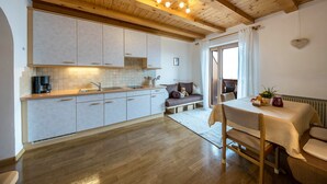 A kitchen with wooden beams, a dining table with chairs, and a view to the outside. - Eichernhof Apartment Marillenblüte – Delicious Vital Breakfast and Dinner Available on Request (Verano)