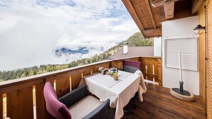 A wooden deck with a table and chairs, a view of a mountain range, and a white door. - Eichernhof Apartment Marillenblüte – Delicious Vital Breakfast and Dinner Available on Request (Verano)