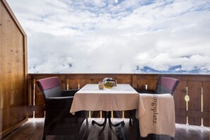 A table with a tablecloth, two chairs, a teapot, and a glass on a balcony with a wooden railing and a view of clouds. - Eichernhof Apartment Marillenblüte – Delicious Vital Breakfast and Dinner Available on Request (Verano)