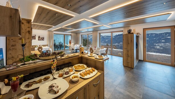 A modern kitchen with a wooden ceiling, a central island with food, and large windows with mountain views. - Eichernhof Apartment Marillenblüte – Delicious Vital Breakfast and Dinner Available on Request (Verano)
