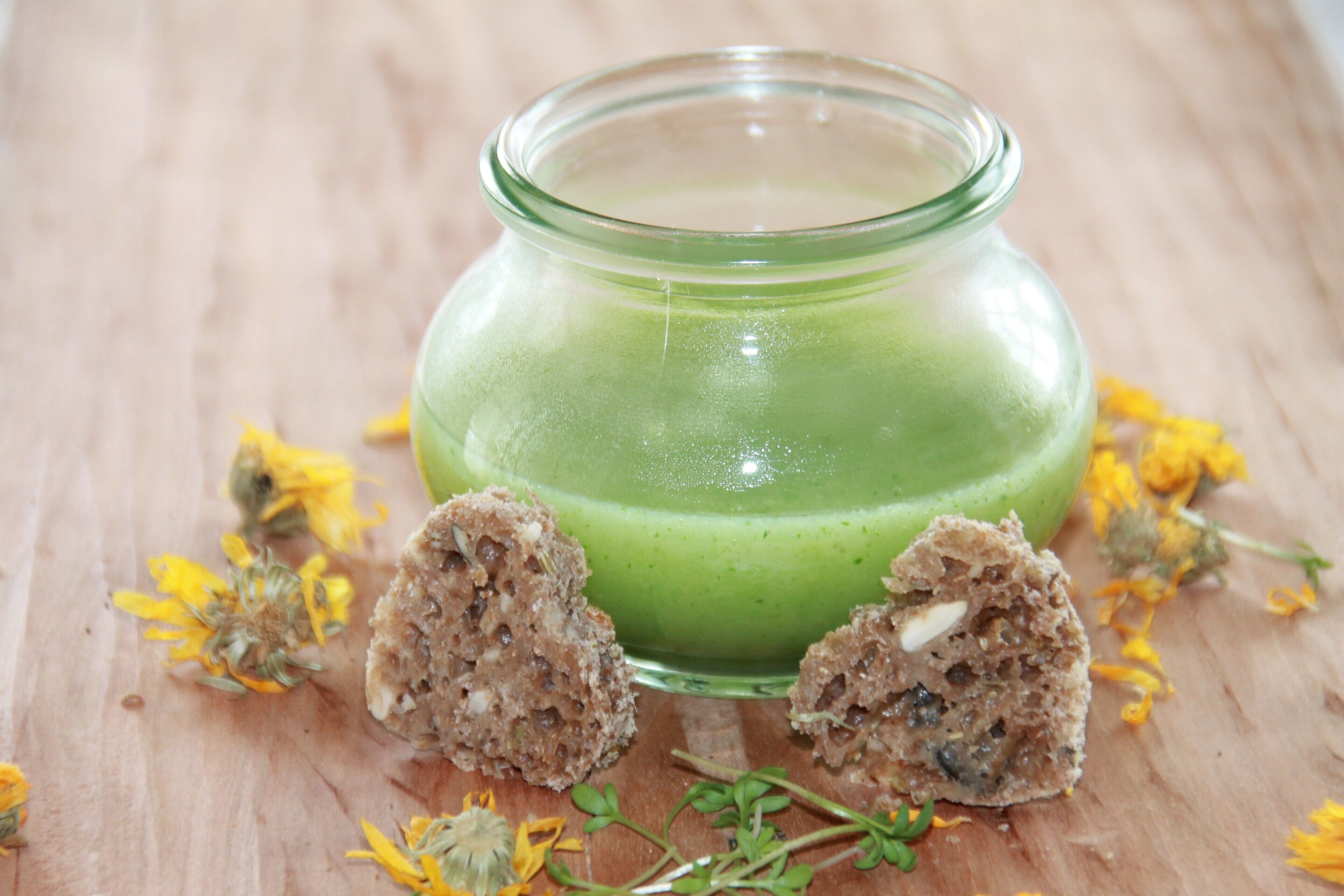 Um frasco de vidro com líquido verde e duas porções de uma substância marrom sobre uma superfície de madeira.