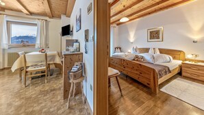 A wooden interior with a dining area, a bed with a nightstand, and a window with a mountain view. - Eichernhof Apartment Kirschblüte – Delicious Vital Breakfast and Dinner Available on Request (Verano)