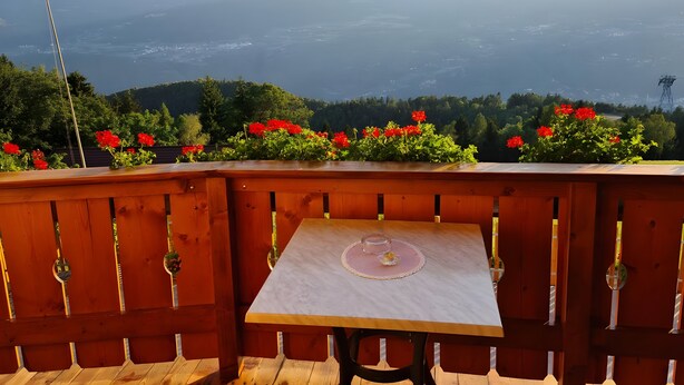 A wooden deck with a table and chairs, overlooking a mountainous landscape with red flowers in the foreground. - Eichernhof Apartment Kirschblüte – Delicious Vital Breakfast and Dinner Available on Request (Verano)