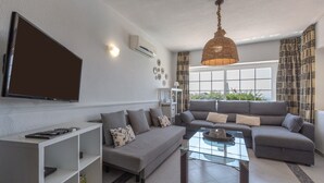 A modern living room with a sofa, a coffee table, a TV mounted on the wall, and a large window with curtains. - Villa 'Del Sol - Entre Tu y Yo' with Sea View, Heated Pool, 3 Terraces & Wi-Fi (Benalmádena)