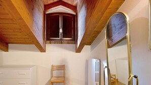 Una habitación con techo inclinado, una silla de madera, un radiador blanco y un espejo.