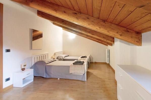 Une chambre avec un plafond en bois, un lit, une table de chevet, une commode et un radiateur.