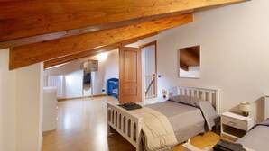 Un dormitorio con techo inclinado, cama, mesita de noche, cómoda y radiador.