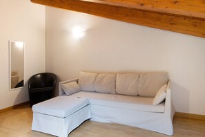 Un canapé d’angle blanc avec un pouf assorti, un fauteuil noir et un plafond en bois.