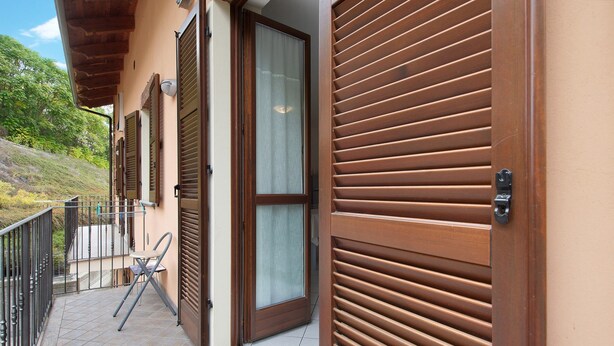 Un balcón con una silla, una puerta con ventana y vista a una ladera.