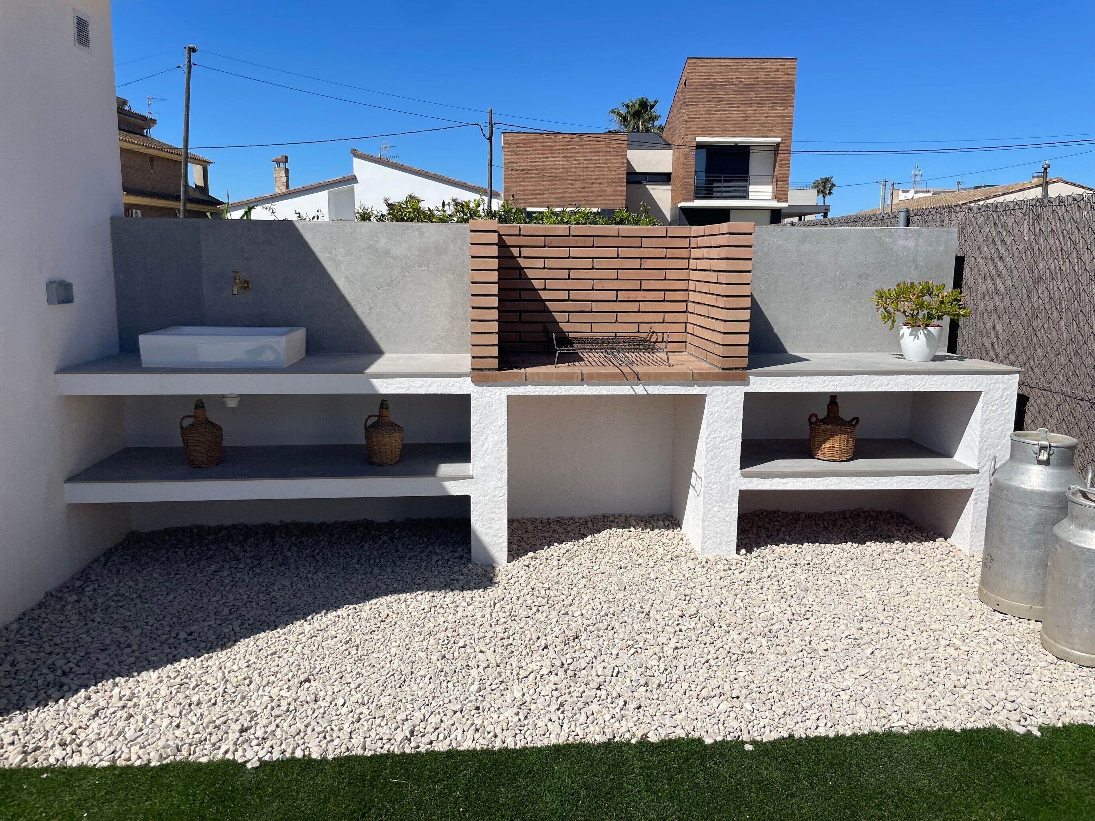 Una cocina exterior moderna con un lavadero, parrilla y estantes de almacenamiento.