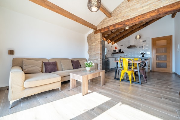 A living room with a sofa, a coffee table, and a kitchen area visible through an open archway.
