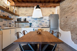 A kitchen with a wooden table, chairs, a hanging light, and a brick wall.