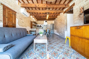 A cozy living area with a sofa, a small table, a wooden cabinet, and a kitchen in the background.