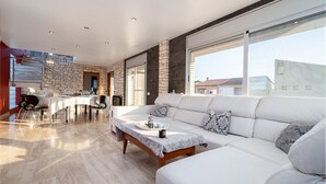 A spacious living area with a large white sofa, a dining table, and a stone accent wall. - Villa 'Luxury Rock Tirri' with Private Pool, Covered Terrace, and Wi-Fi (Reus)
