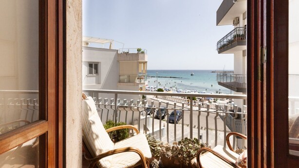 A balcony with wicker chairs, a potted plant, and a view of the beach and sea. - GuestHost - Bella Vista Apartment with balcony SEA VIEW (Otranto)