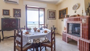A dining area with a table set for four, a fireplace, and a balcony with a view. - GuestHost - Bella Vista Apartment with balcony SEA VIEW (Otranto)