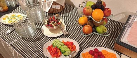 A buffet table with various food items, including fruits, vegetables, and a salad.