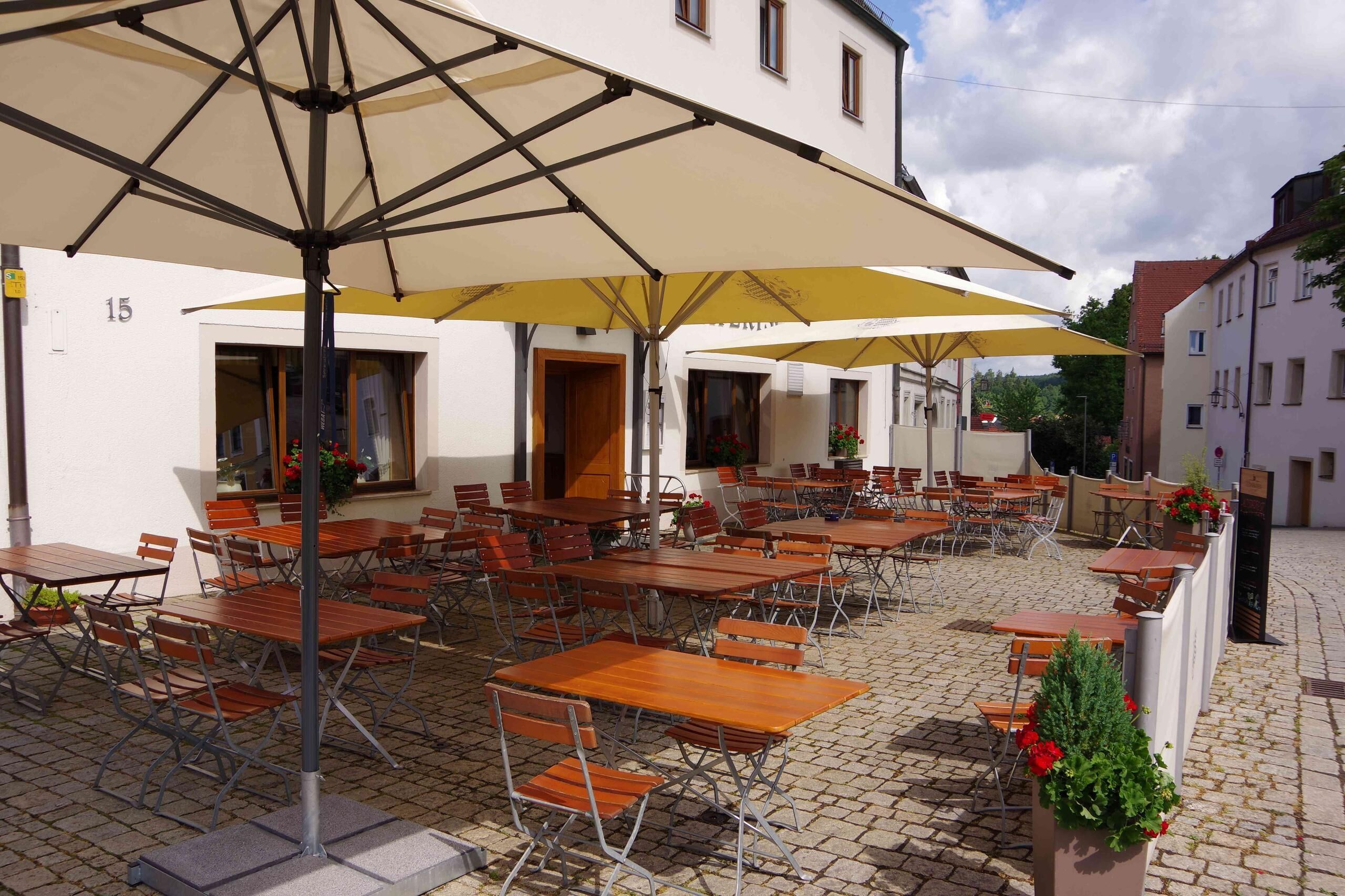 Un café al aire libre con varias mesas y sillas, sombrillas y suelo adoquinado.