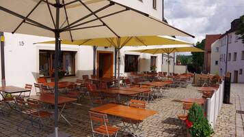 Un café al aire libre con varias mesas y sillas, sombrillas y suelo adoquinado.