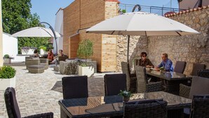 An outdoor patio with wicker furniture and umbrellas, stone walls, and a wooden building in the background. - Hotelgasthof Bayerischer Hof (Sulzbach-Rosenberg)
