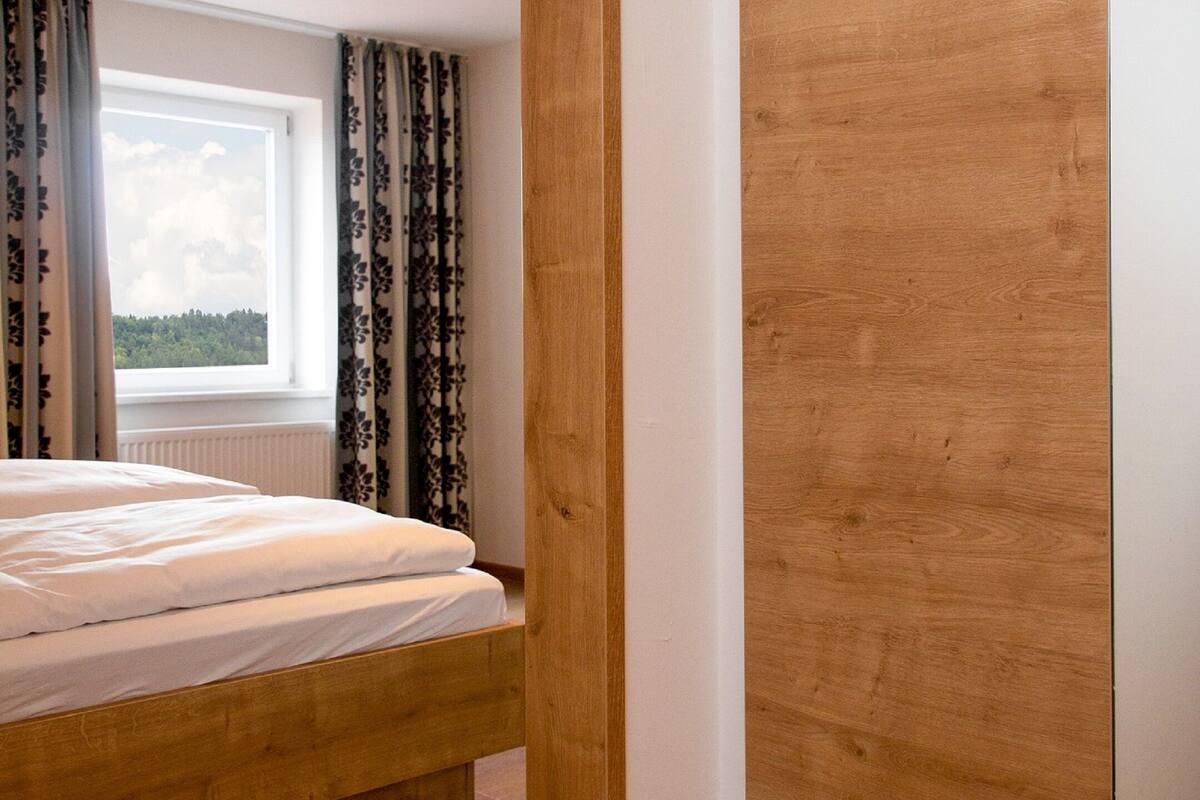 A bedroom with a wooden bed, a large window with curtains, and a wooden wardrobe.