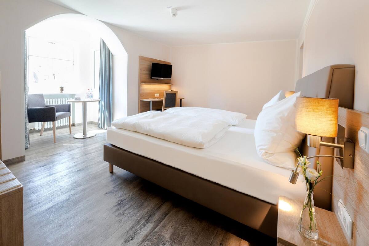 A modern hotel room with a large bed, a desk, a television, and a view of the outside.