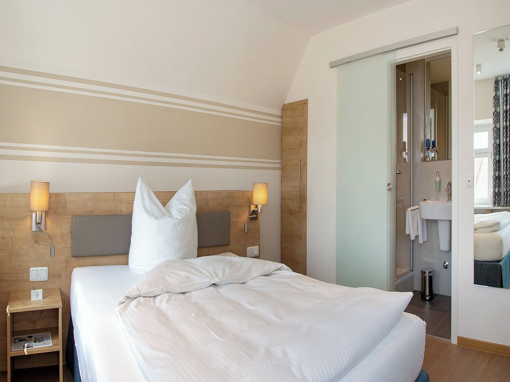 A hotel room with a large bed, bedside lamps, a wooden headboard, and a bathroom visible through an open door.