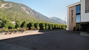 A modern building with 'WALHOF' signage, surrounded by a landscaped area with trees and a mountain backdrop.