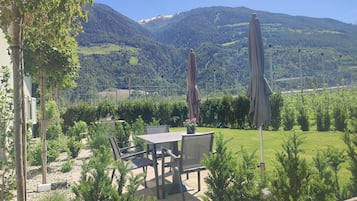 Une terrasse aménagée avec du mobilier d’extérieur, une table et des chaises, entourée de verdure et offrant une vue sur une chaîne de montagnes.
