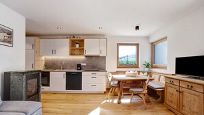 A modern kitchen with white cabinets, a dining area with wooden furniture, and a large window with a view.