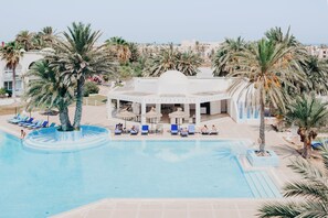 A pool area with lounge chairs and palm trees, surrounded by buildings. - Hotel Bougainvillier Djerba (Djerba Midun)