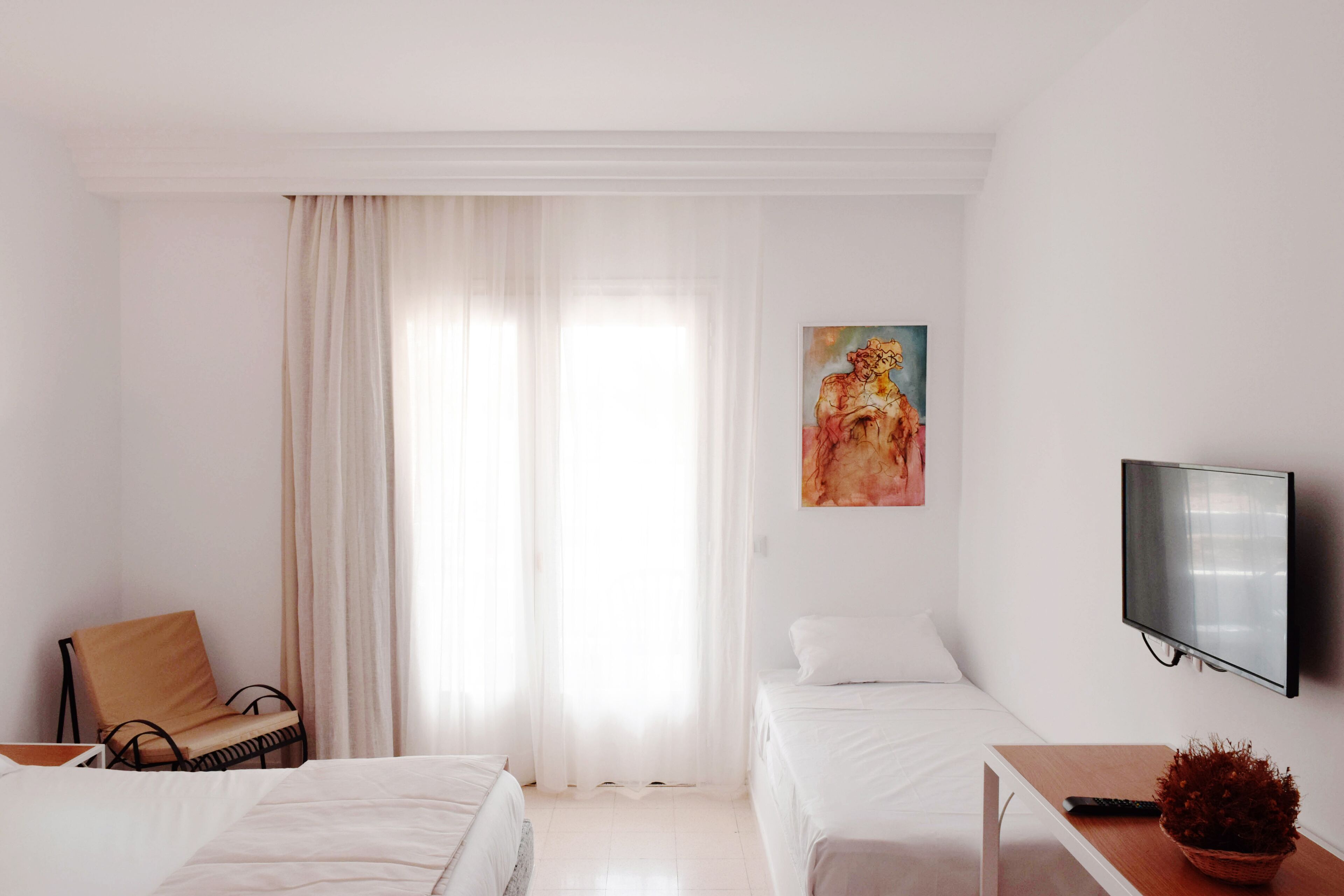 A hotel room with two beds, a chair, a TV, and a painting on the wall.